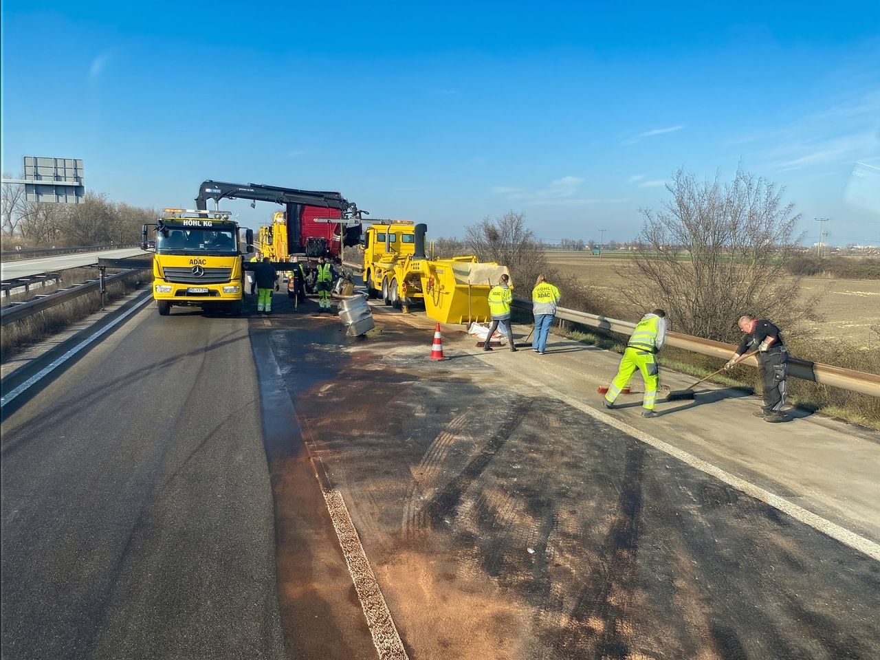 Mitarbeiter reinigen eine Unfallstelle auf der Autobahn, Ölspurfahrzeuge im Hintergrund